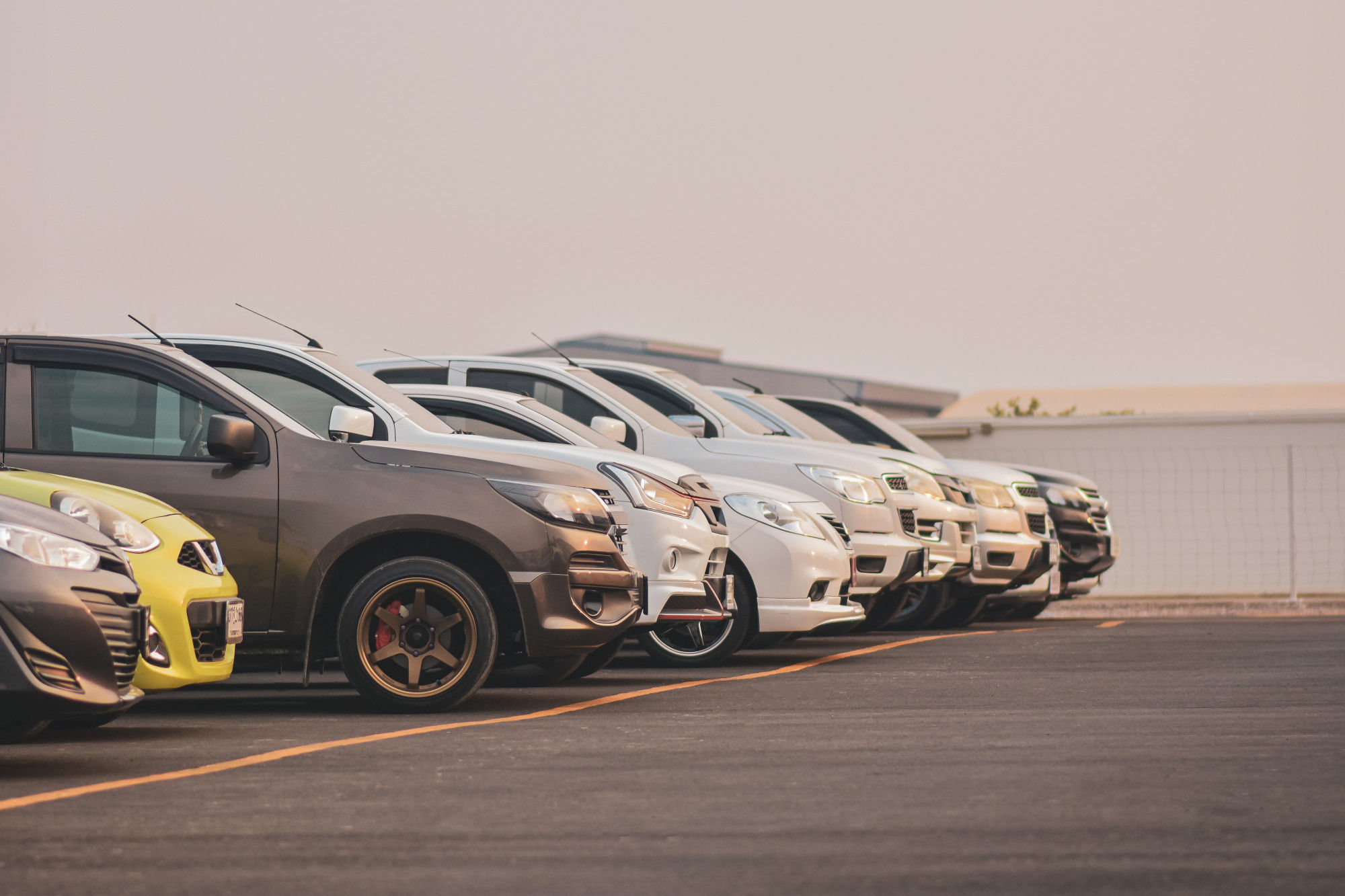 Several cars parked in a straight line within a spacious parking lot, showcasing organized vehicle placement.