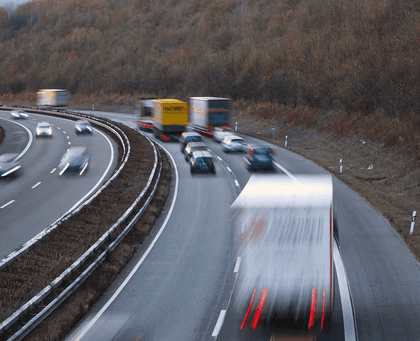Blurred motion of trucks and cars driving on a multi-lane highway through a hilly area.