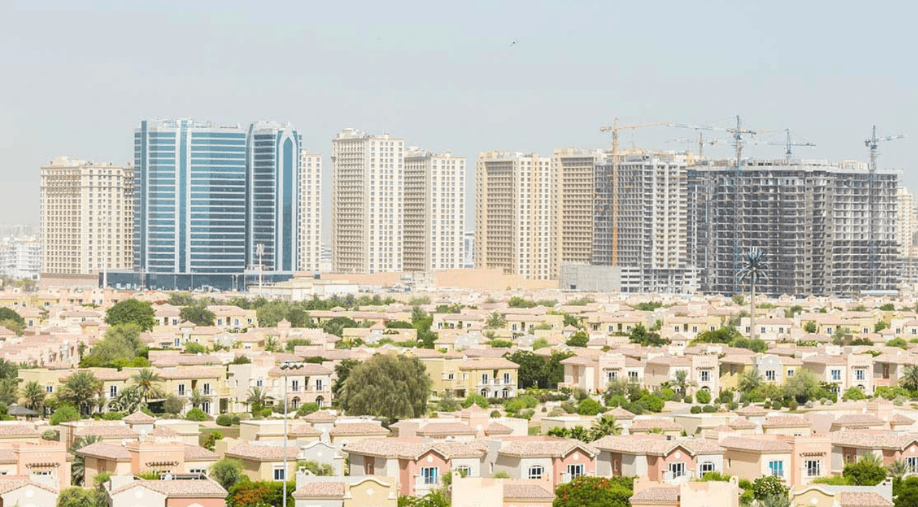 A skyline of Dubai Sports City featuring numerous tall buildings against a clear blue sky.