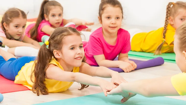Children taking part in a group exercise activity on colourful floor mats.