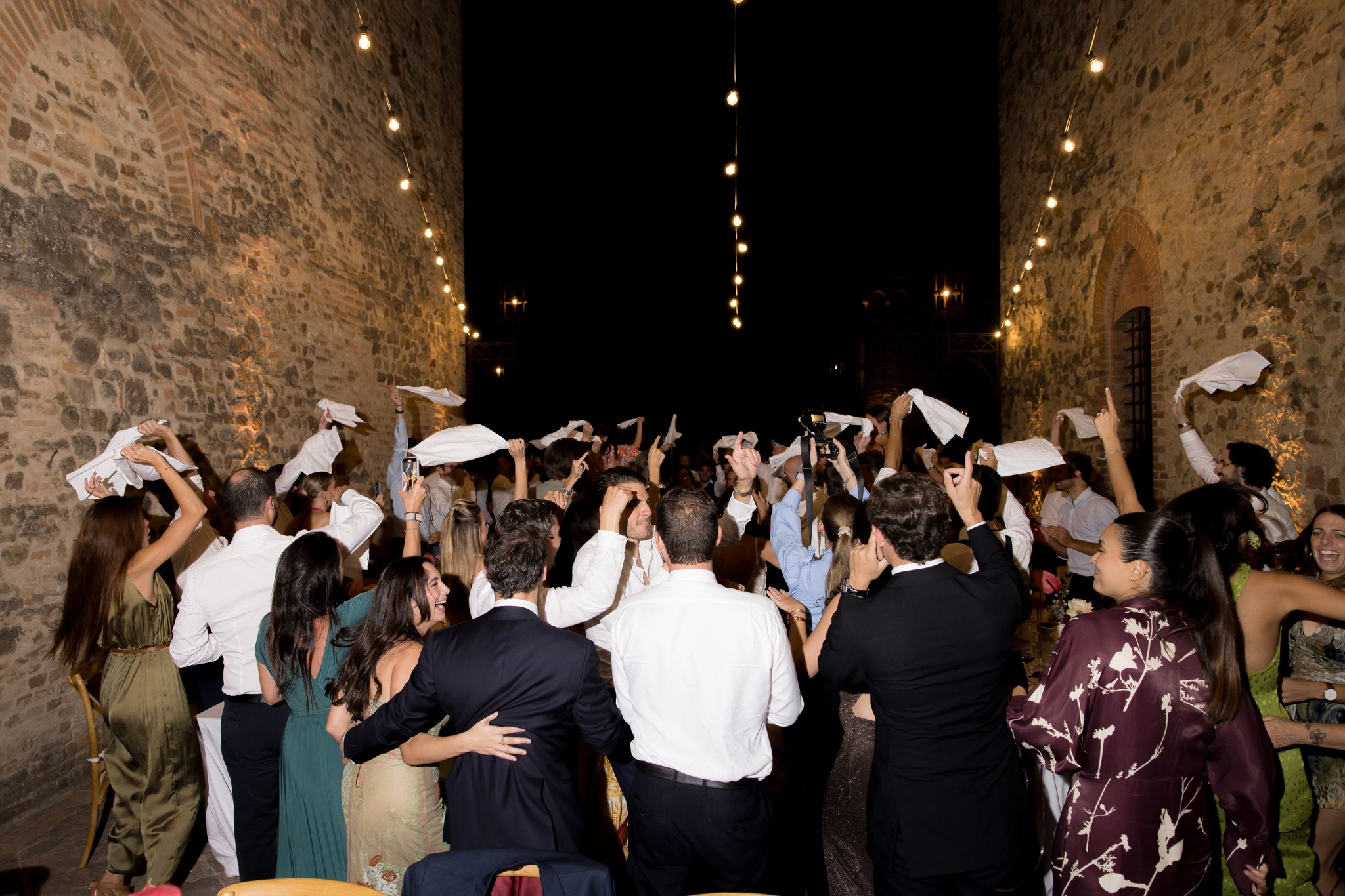 Ospiti ballano sotto le volte del Castello di Tabiano con coriandoli bianchi nel ricevimento matrimoniale notturno