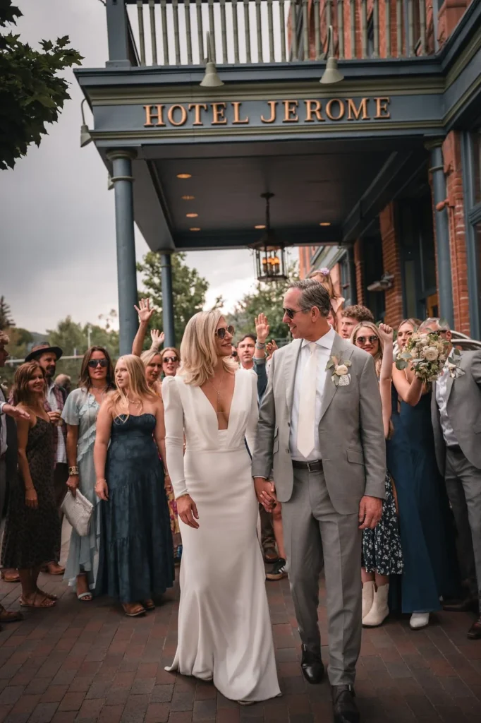Newlyweds walking beneath the Hotel Jerome sign with guests behind them