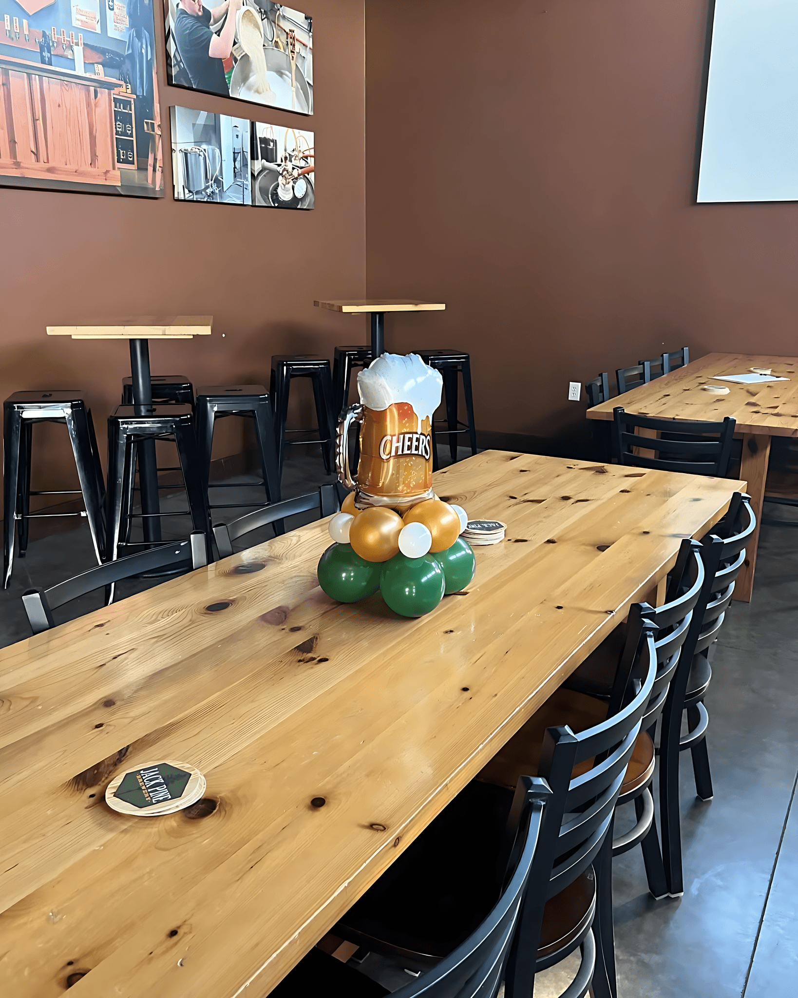 Long wooden table decorated with balloon centerpieces and event décor in a modern indoor space by Be Bold Balloons
