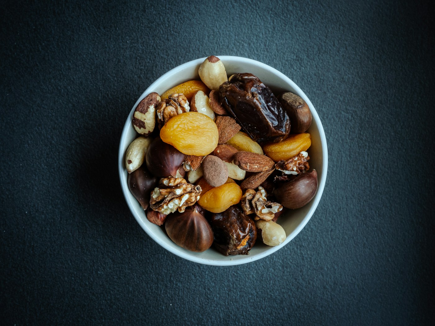A white bowl filled with a mix of walnuts, almonds, cashews and dried fruit, a heart-healthy snack of nuts and fruit
