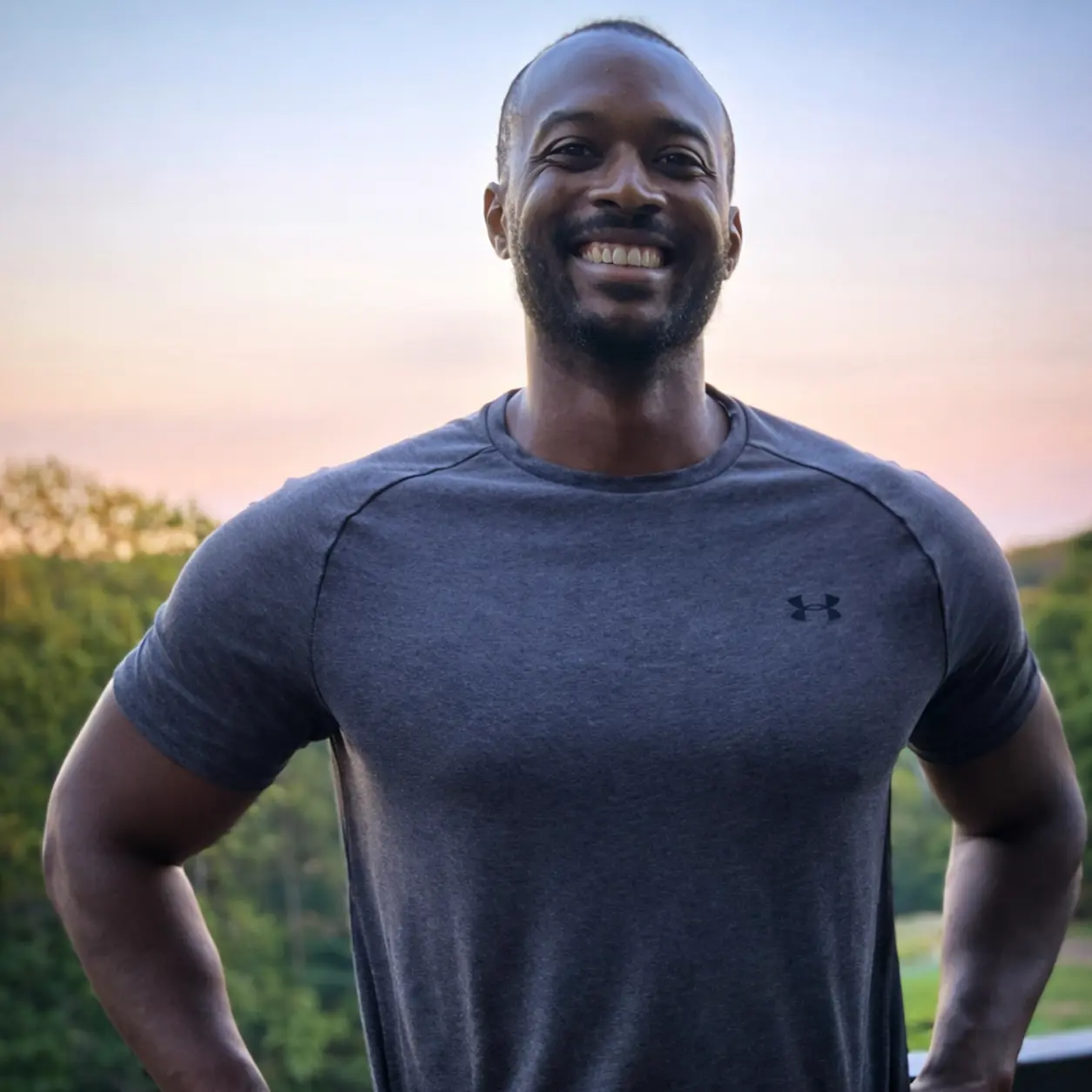 Josiah C standing outdoors and smiling, wearing a gray athletic shirt with a scenic background.