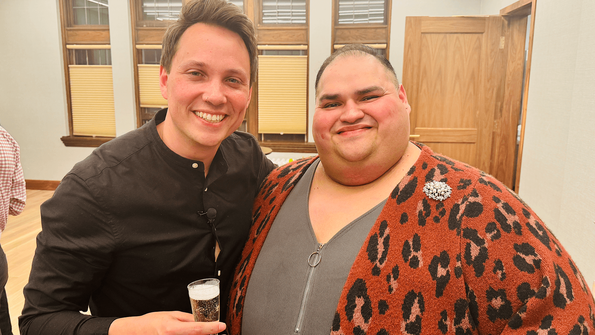 Two friends smiling together during an event at Grace Trinity Church, one holding a glass of champagne.