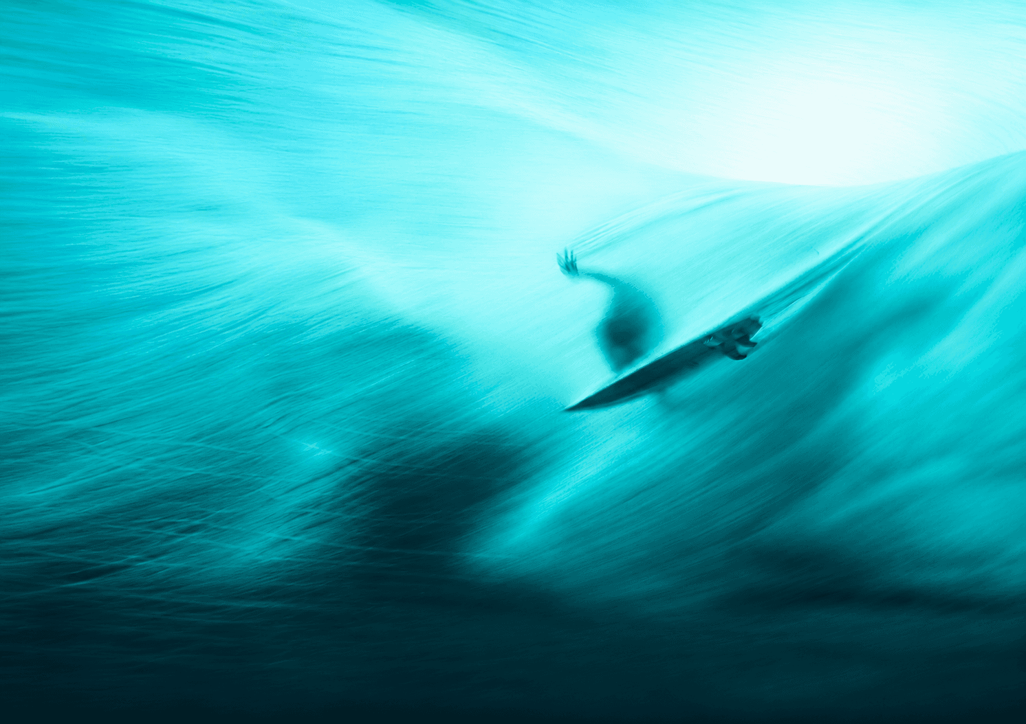 A surfer carving through a breaking wave, captured with heavy motion blur in vivid turquoise.