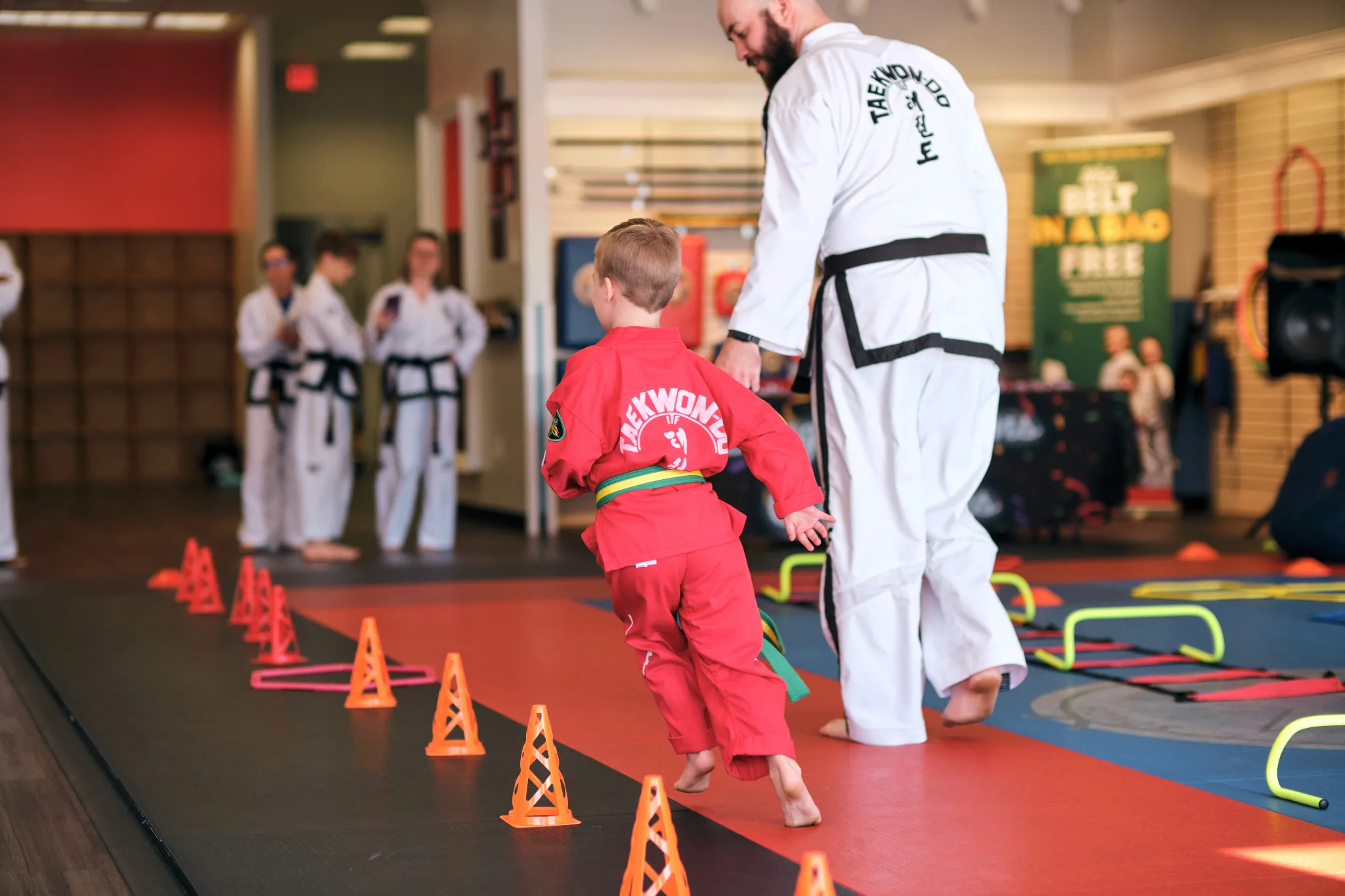 Young martial arts student in colored gi with instructor demonstrate techniques on a obstical course on the mat in an indoor dojo.