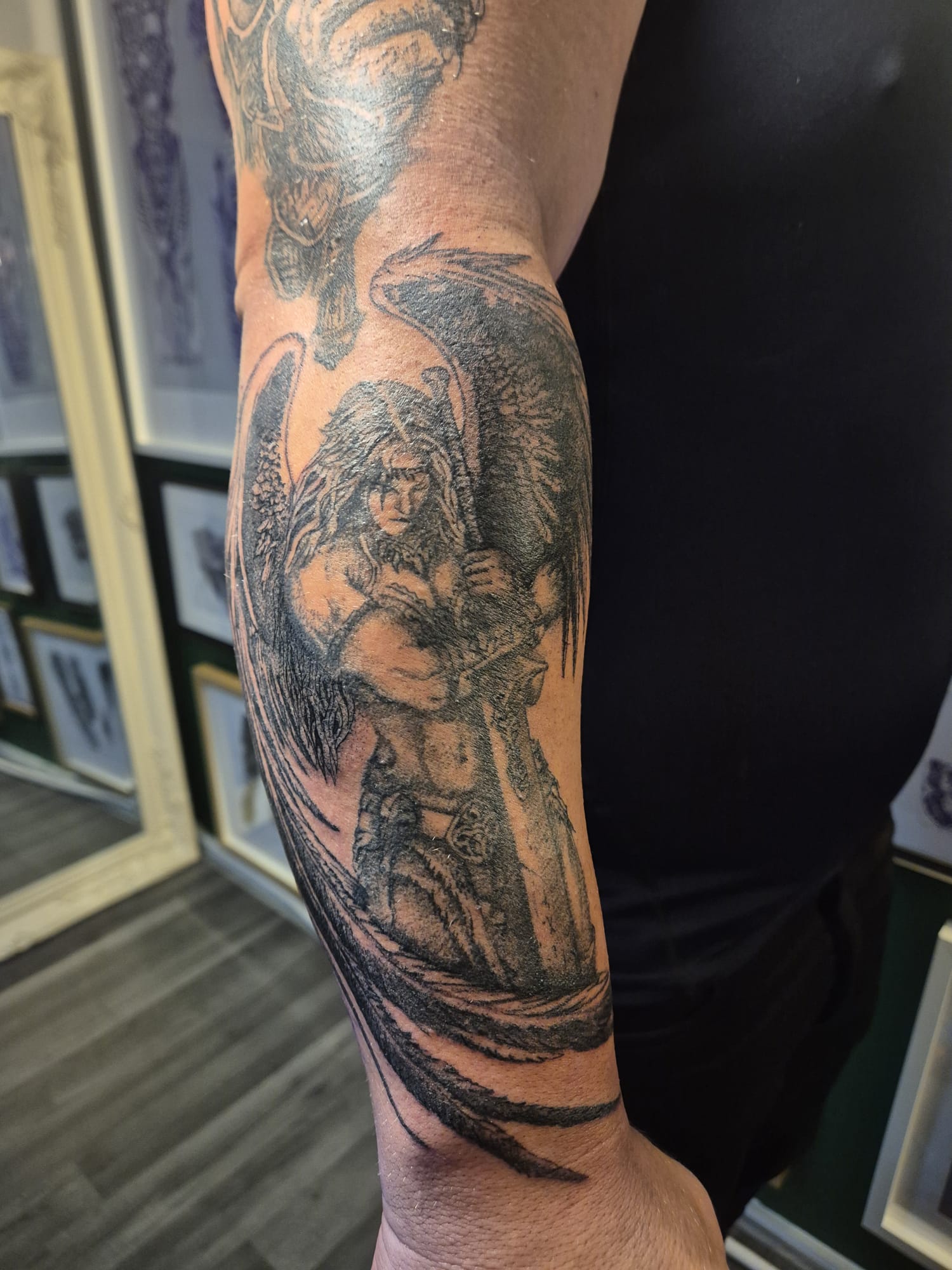 Black and grey angel tattoo on forearm with wings and sword design