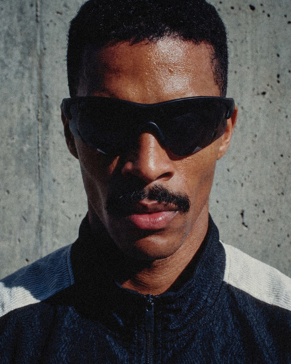 Close-up of a man with a mustache wearing dark athletic sunglasses.