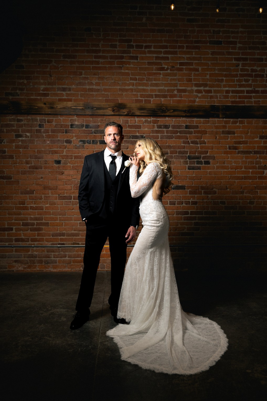 A couple in wedding attire walks hand in hand across a sunlit field.