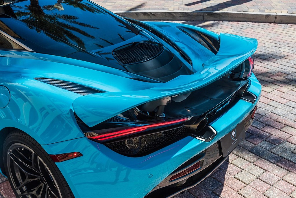 A stunning blue McLaren 720S with dihedral doors open, parked in a luxurious setting with palm trees and an elegant building in the background. This exotic supercar features a sleek design, powerful twin-turbo V8 engine, and unparalleled performance, making it the perfect choice for a luxury car rental experience.