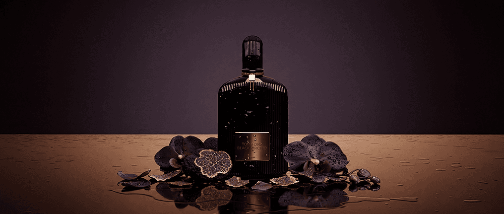 Luxury product commercial still of Tom Ford Black Orchid perfume bottle with water droplets, flanked by dark purple orchids and a sliced black truffle by Atomic Models creative studio.