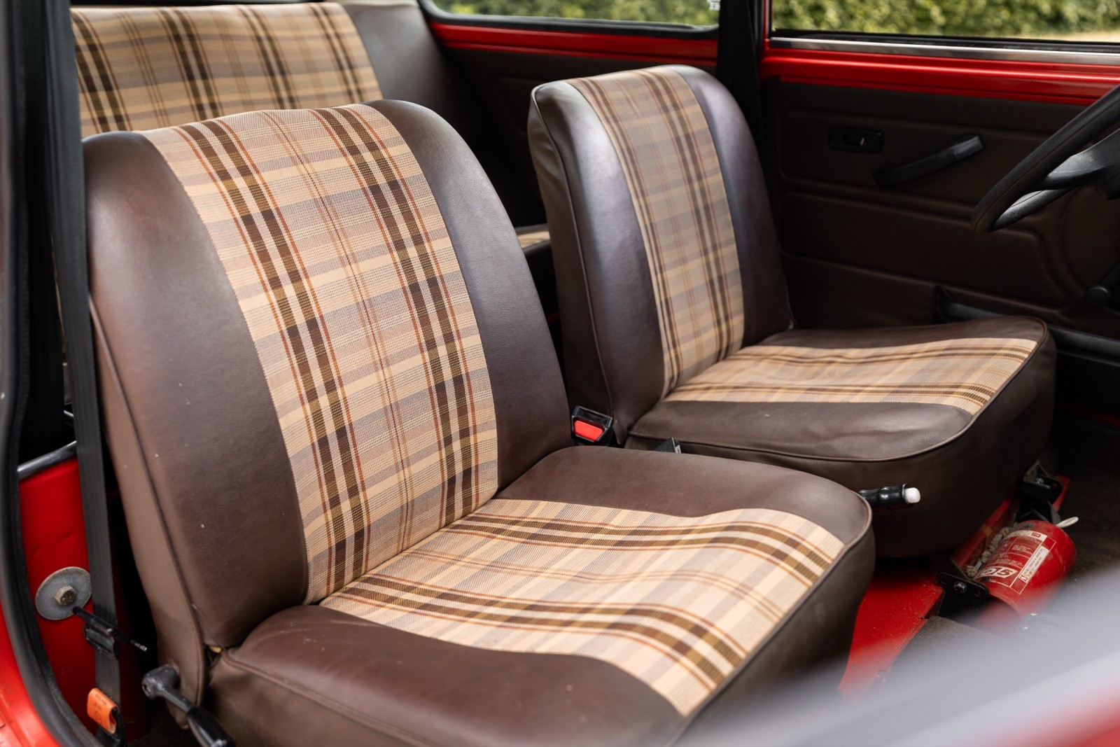 Image of two retro plaid seat covers on brown car seats, set against a red interior backdrop.