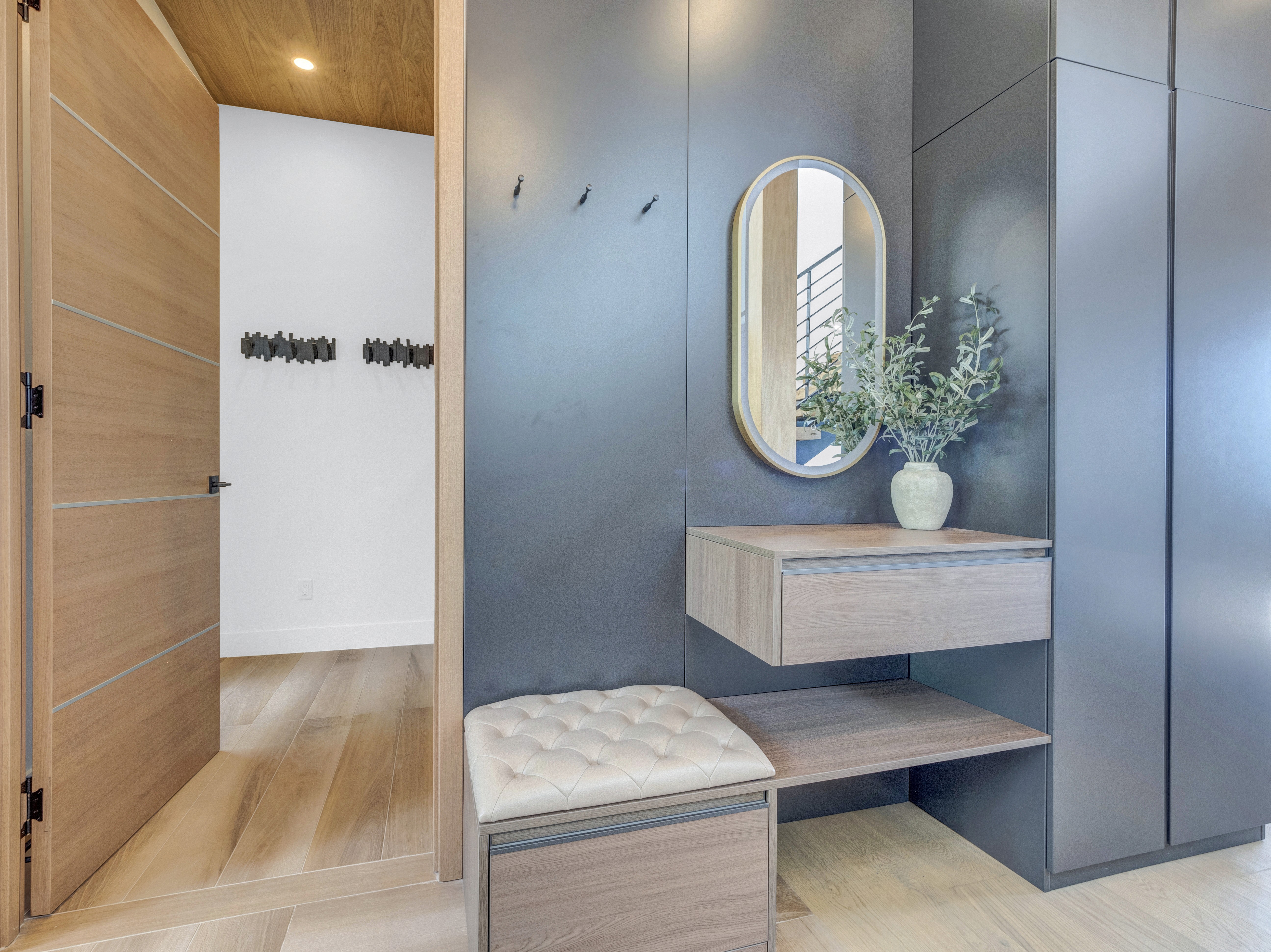 Close-up of custom entryway cabinetry featuring a floating wood drawer, oval mirror, and a tufted leather bench seat
