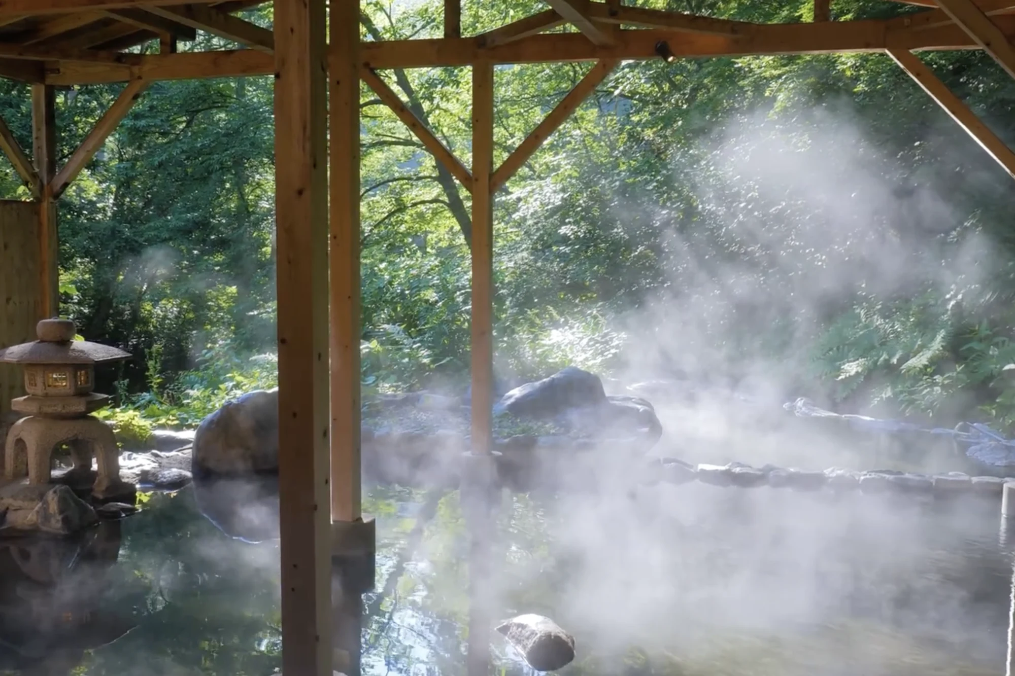 An outdoor hot spring bath steaming among autumn trees at a Kinosaki inn.
