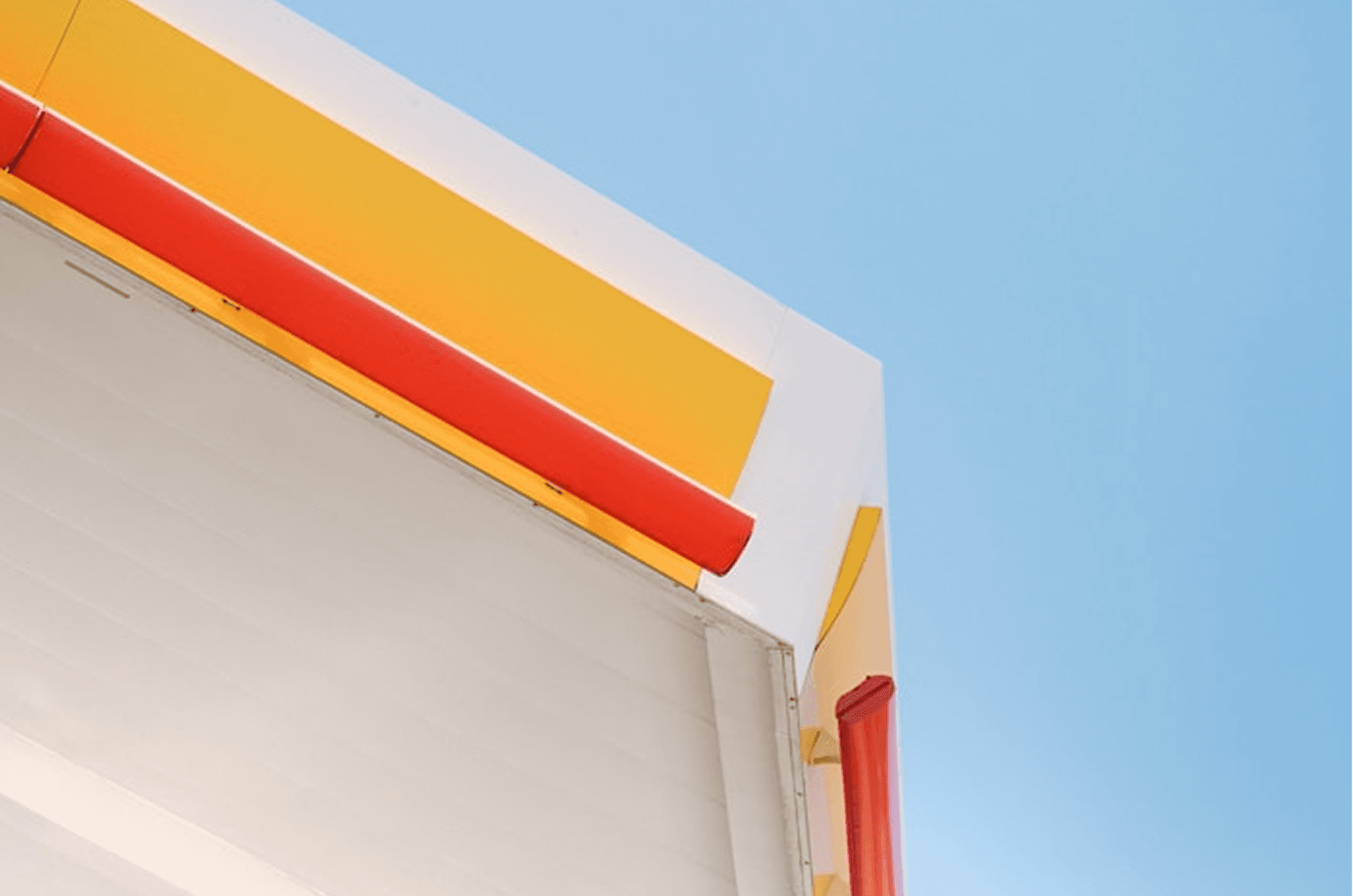 Minimalist architectural detail featuring bold yellow, red, and white geometric building elements against a clear blue sky—modern urban design with clean lines and vibrant contemporary colors.