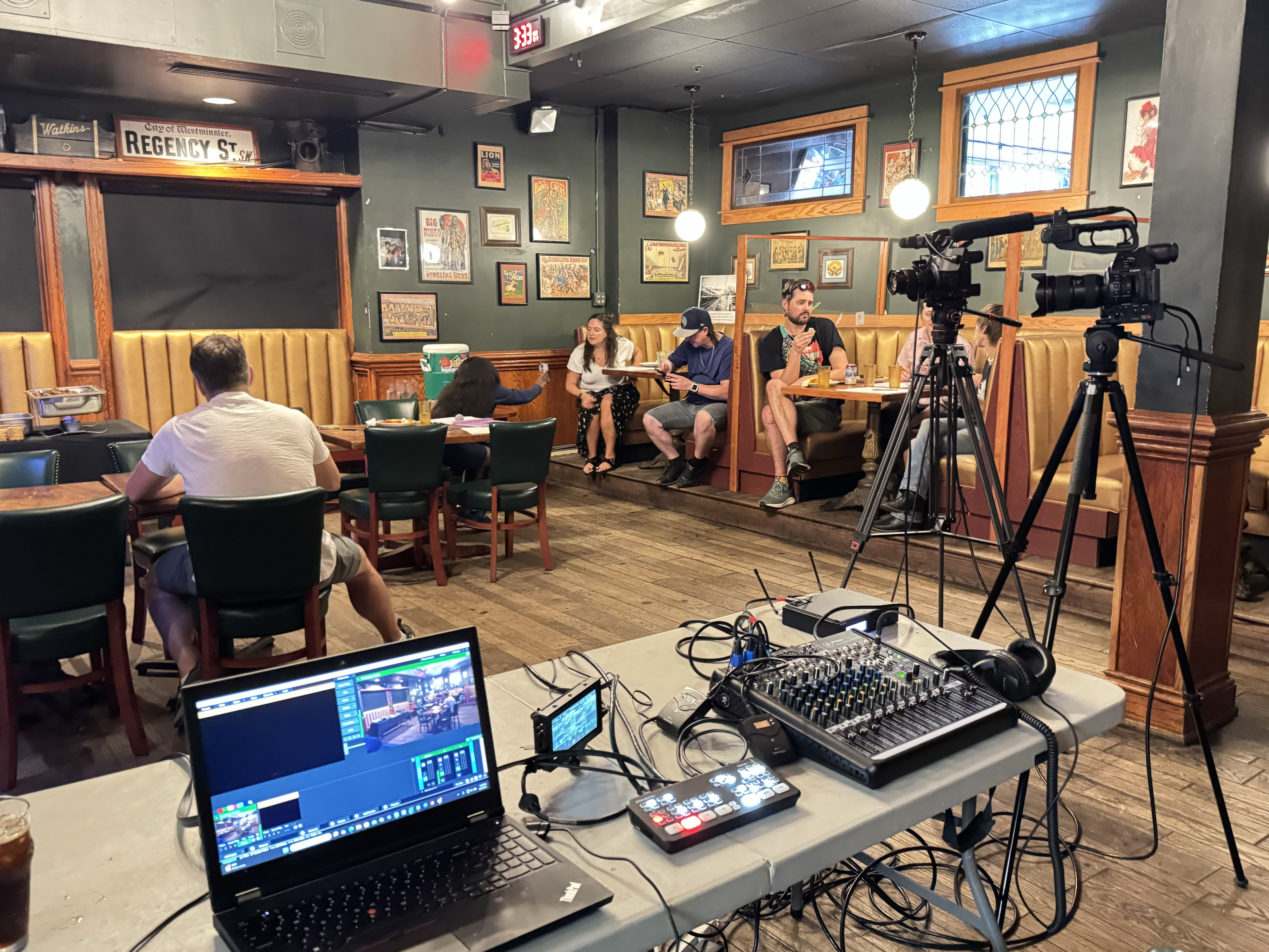 Live video production setup inside a restaurant with cameras on tripods, a mixing board, and monitoring laptop.