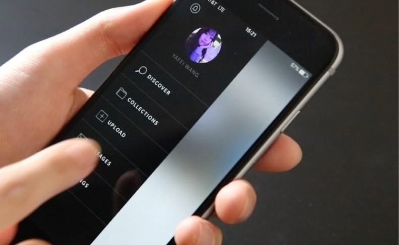 A hand holds a smartphone displaying the TikTok app interface. The screen shows a circular profile picture of a young person with dark hair, labeled “YAFEI WANG.” The app’s navigation menu includes options like “DISCOVER,” “COLLECTIONS,” “UPLOAD,” and “SAGES.” The time displayed on the phone is 16:21, and the battery level is at 57%. The background is dark and out of focus.