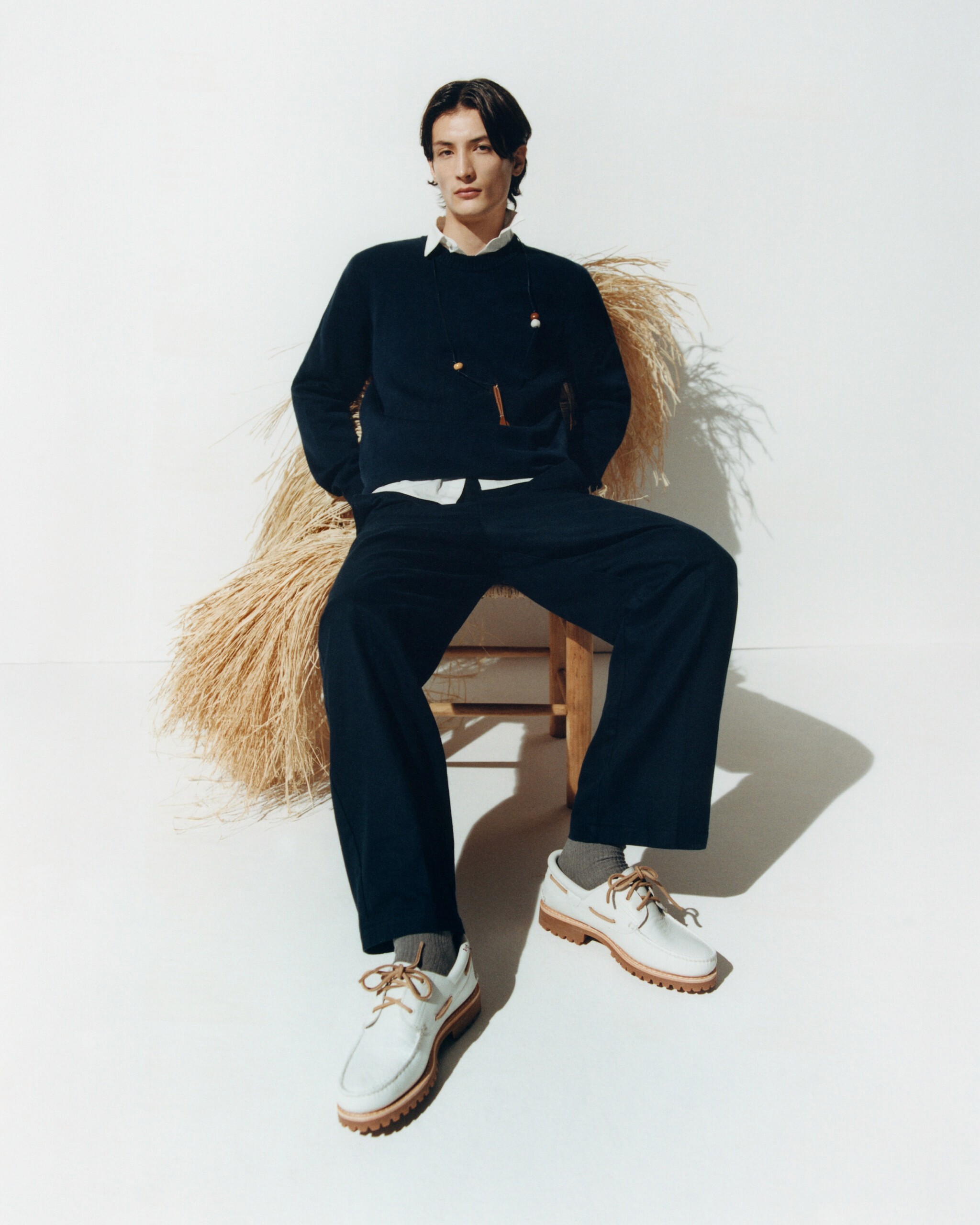 Ce mannequin homme dans le lookbook Thinking Mu porte un pull col V noir et un pantalon en coton noir