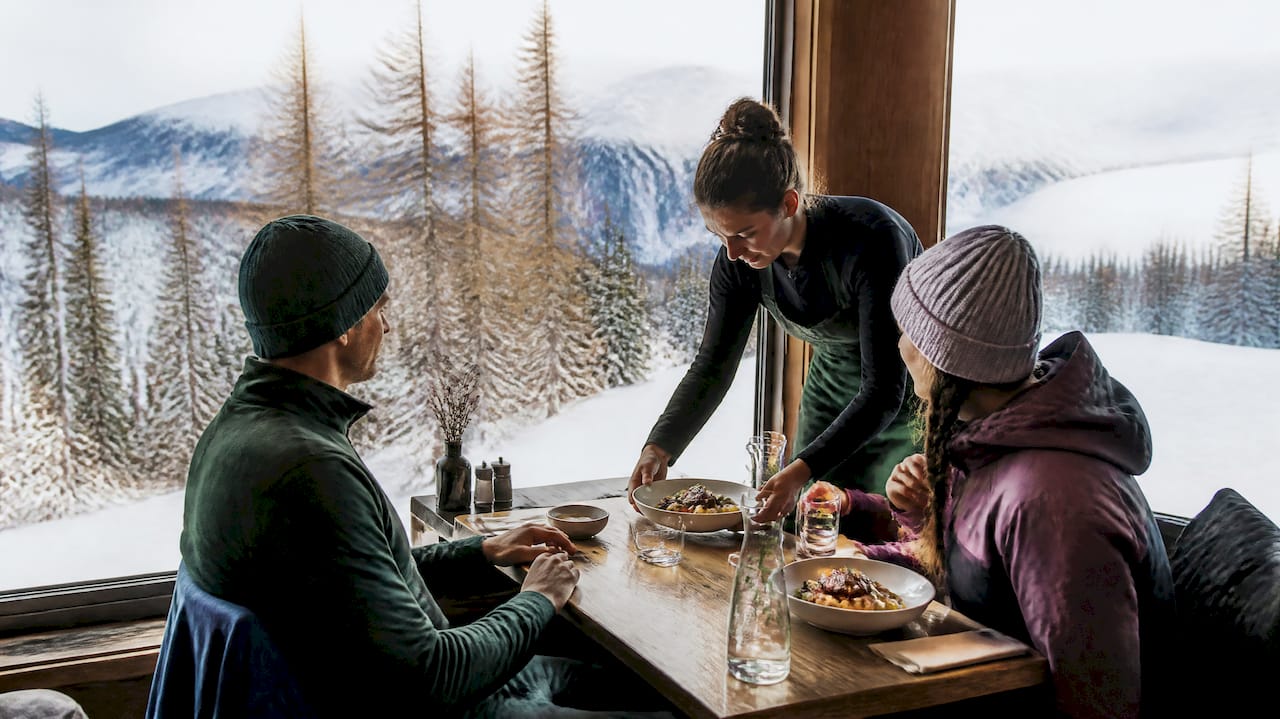 People dining outdoors beside snow-covered mountains