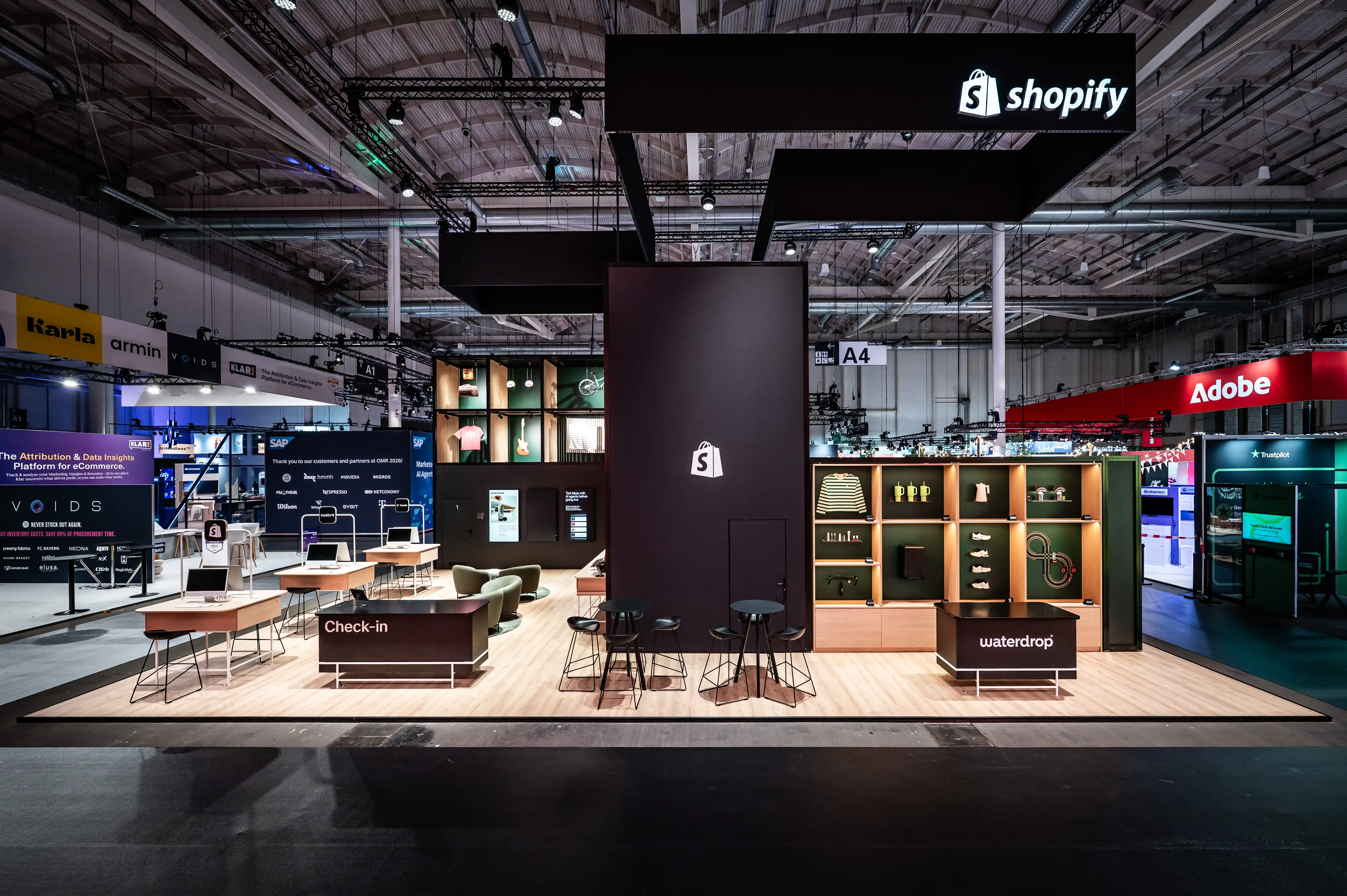 Front view of the dark Shopify booth with check-in counter, waterdrop shelf and illuminated product niches.