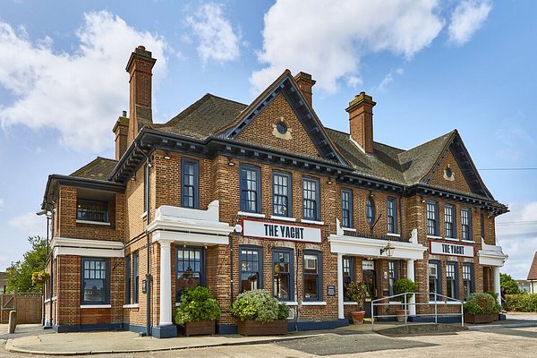 A smiling man with curly hair is sitting at a desk, looking at the camera, with a laptop and a lamp in the background.