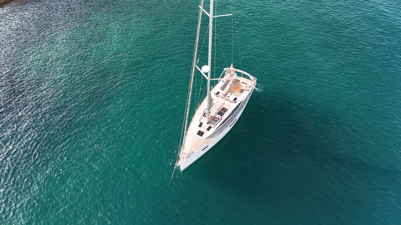 Beneteau Clipper 361 sailing yacht at anchor in Kalkara Creek, Valletta Harbour, Malta, showing the starboard profile with clean white hull, tall aluminium mast, furled sails, bimini and solar panel, with superyachts and the historic Corradino waterfront fortifications visible in the background under a bright summer sky