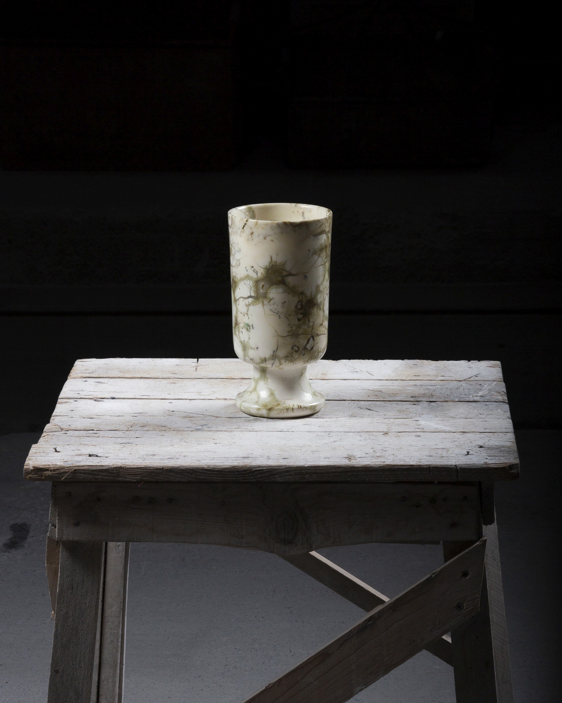 Vase en marbre rare blanc posé sur une table en bois et éclairé par une lampe de chantier hors champs