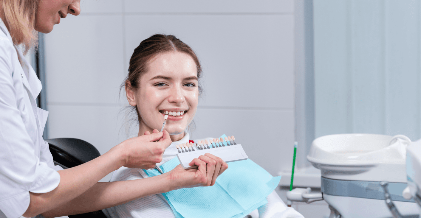 A patient sitting in a dental chair, smiling and holding a model of teeth with braces.