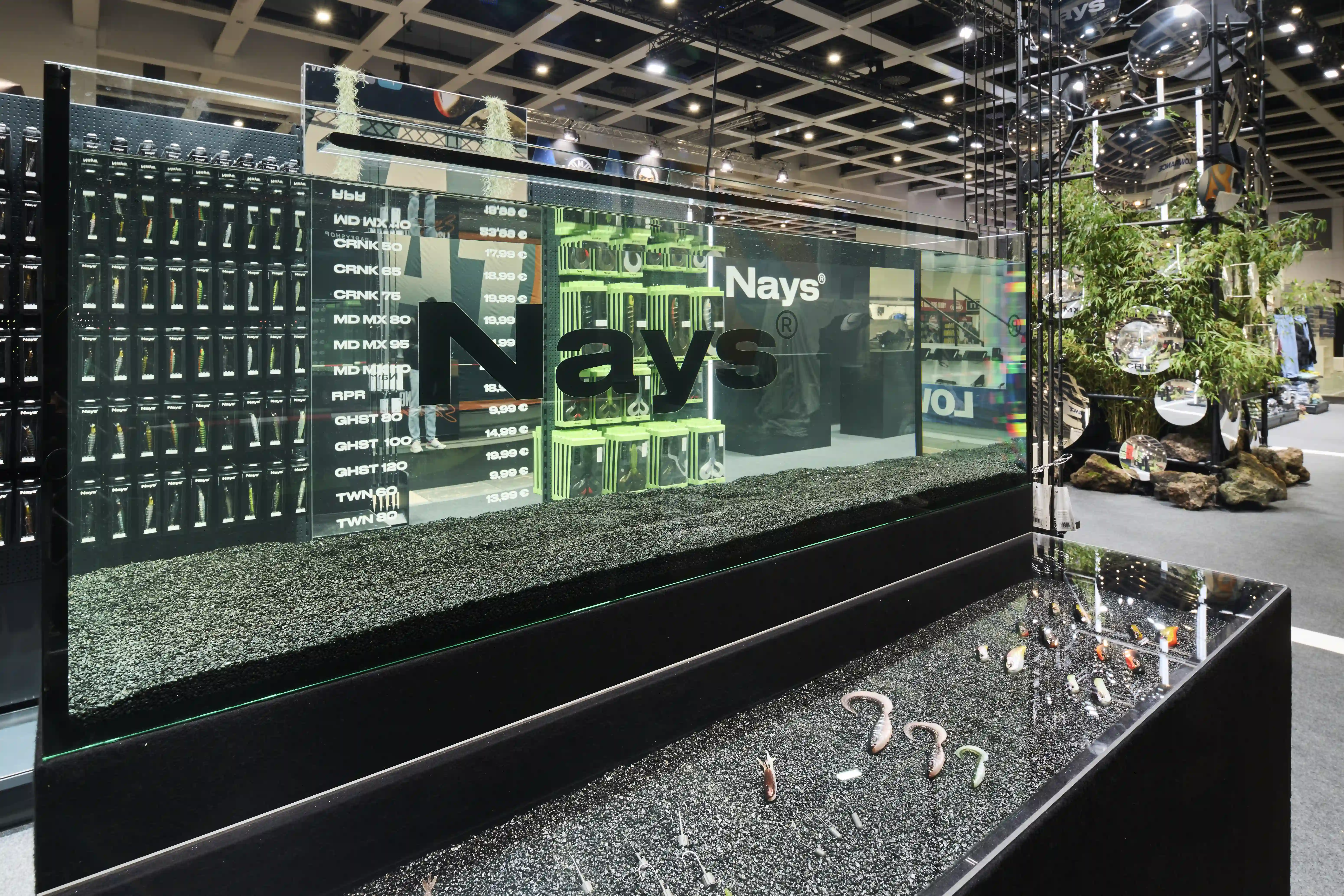 Long aquarium display with dark gravel, price list and Nays lettering on glass at the trade fair booth.