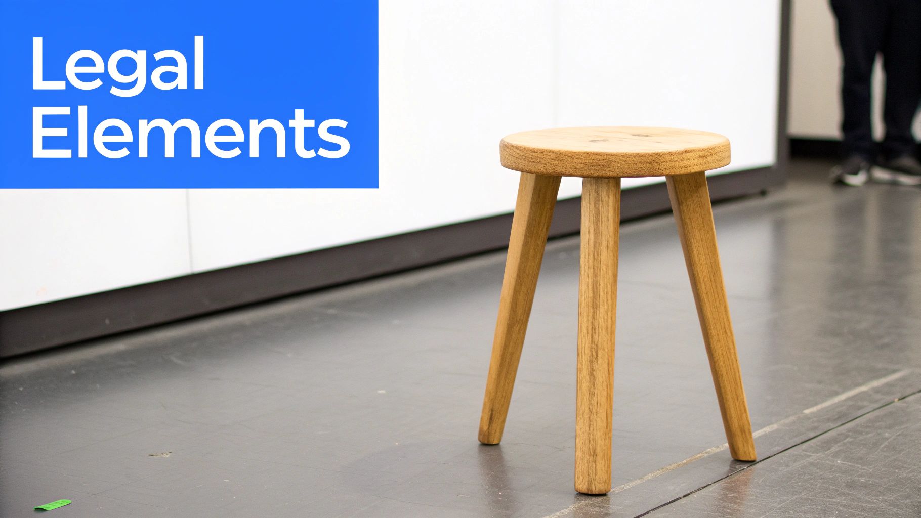 A simple wooden stool stands on a grey floor next to a white wall with a blue 'Legal Elements' sign.