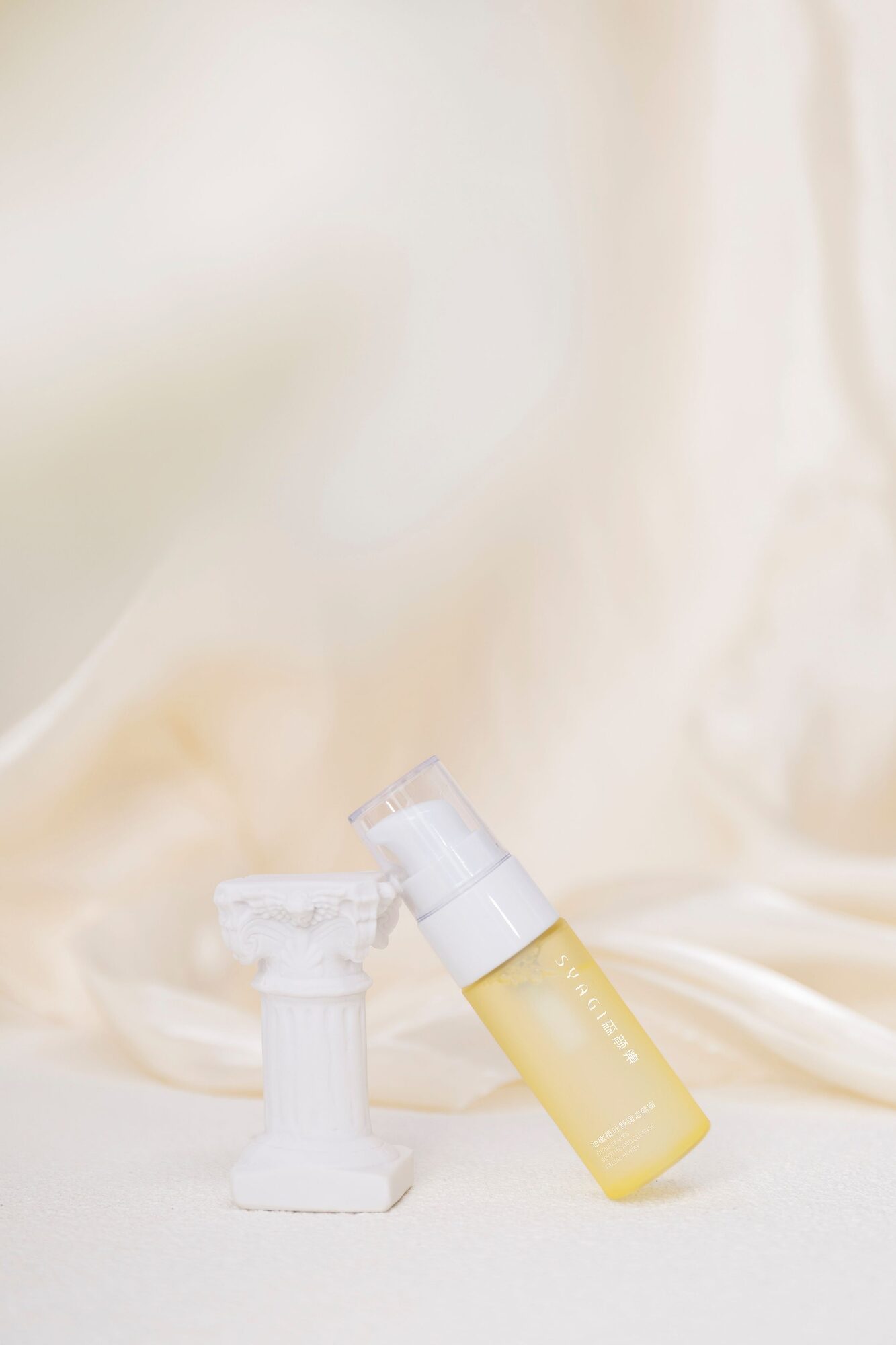 A glass bottle of care product on soft cream fabric