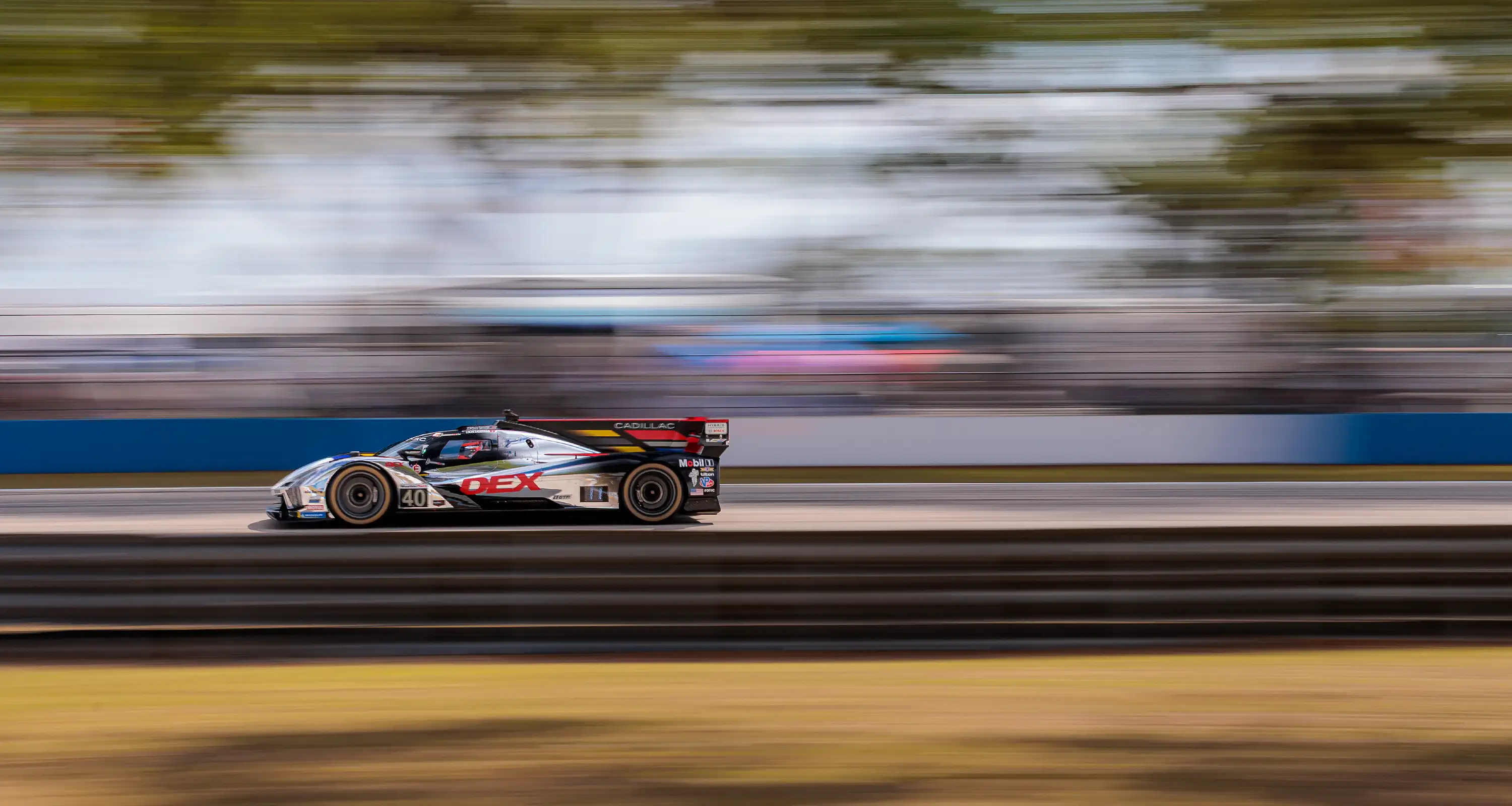 A reflective silver Cadillac race car zooms along a track, emphasizing its speed and striking appearance against the backdrop of the circuit.