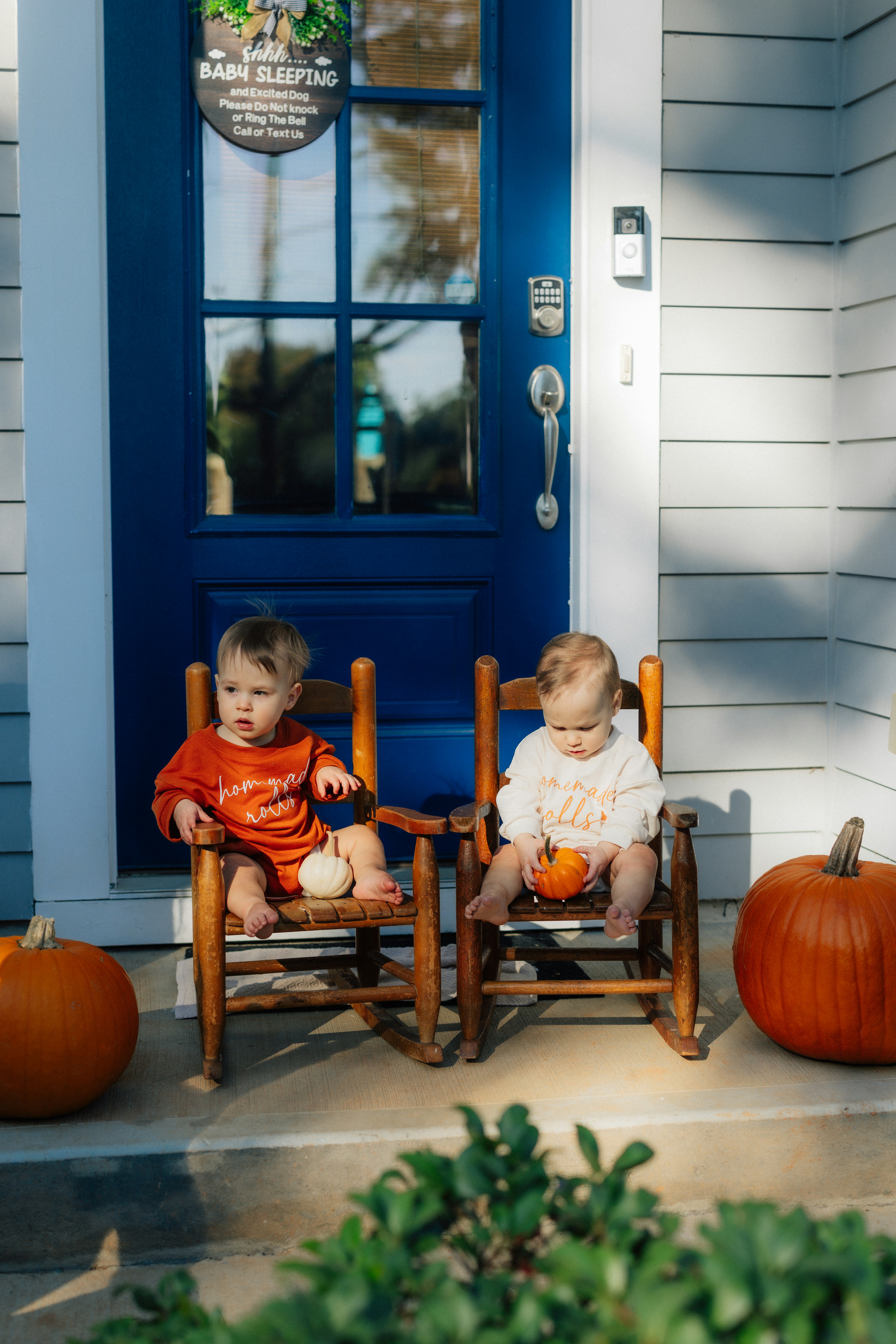 Two babies sitting on chairs with pumpkins.
