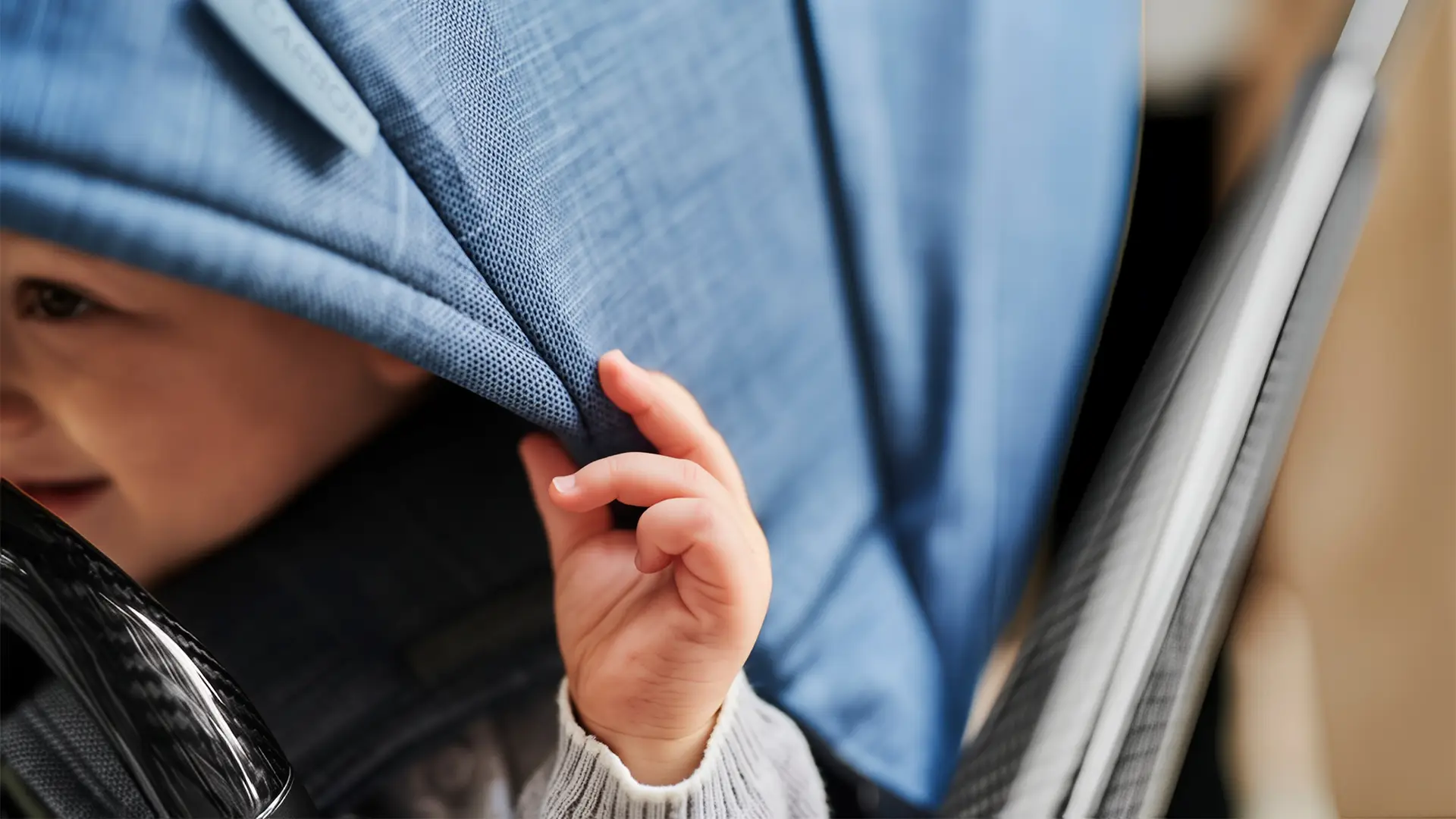 Close-up of a baby’s hand pulling down the fabric canopy of a JUNIORJONES stroller.