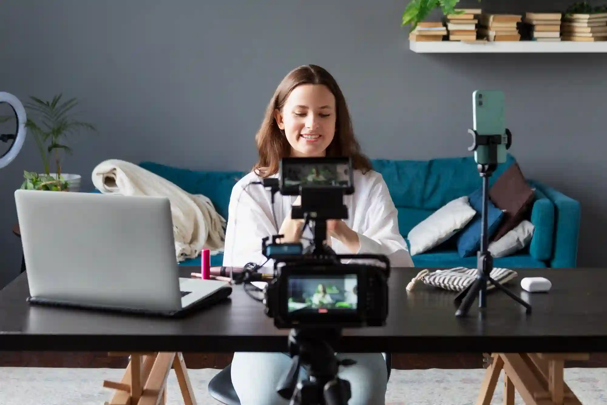 A young woman filming a video with two cameras and a laptop.