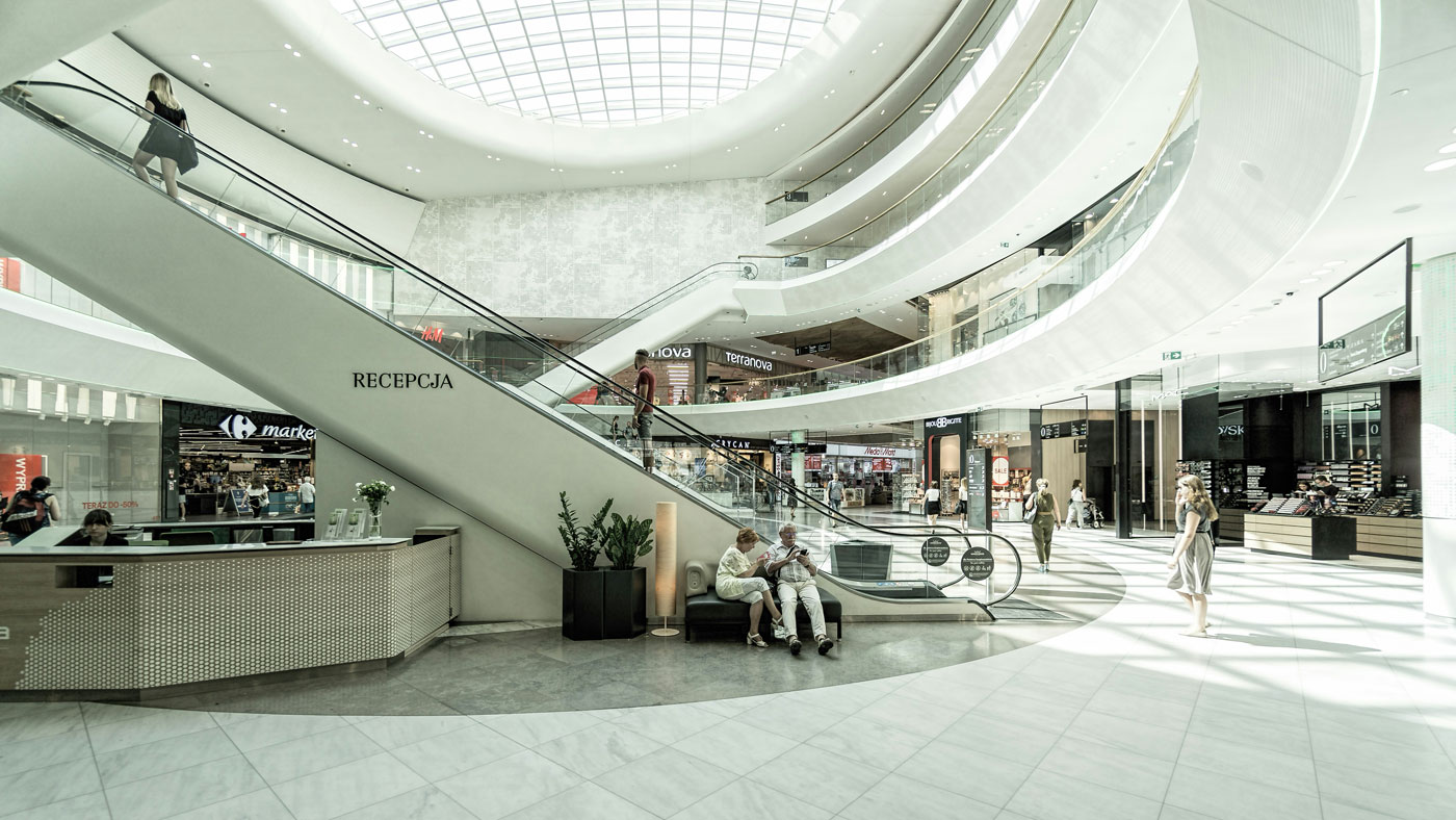 A spacious, modern interior featuring curved architecture, open areas, and escalators in bright lighting.