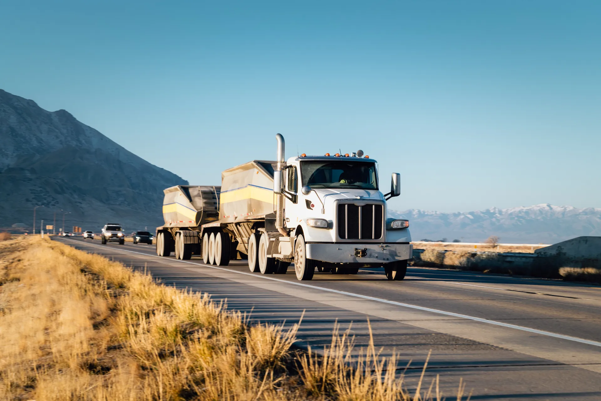 White semi-truck with trailer driving on a mountain highway during daylight.