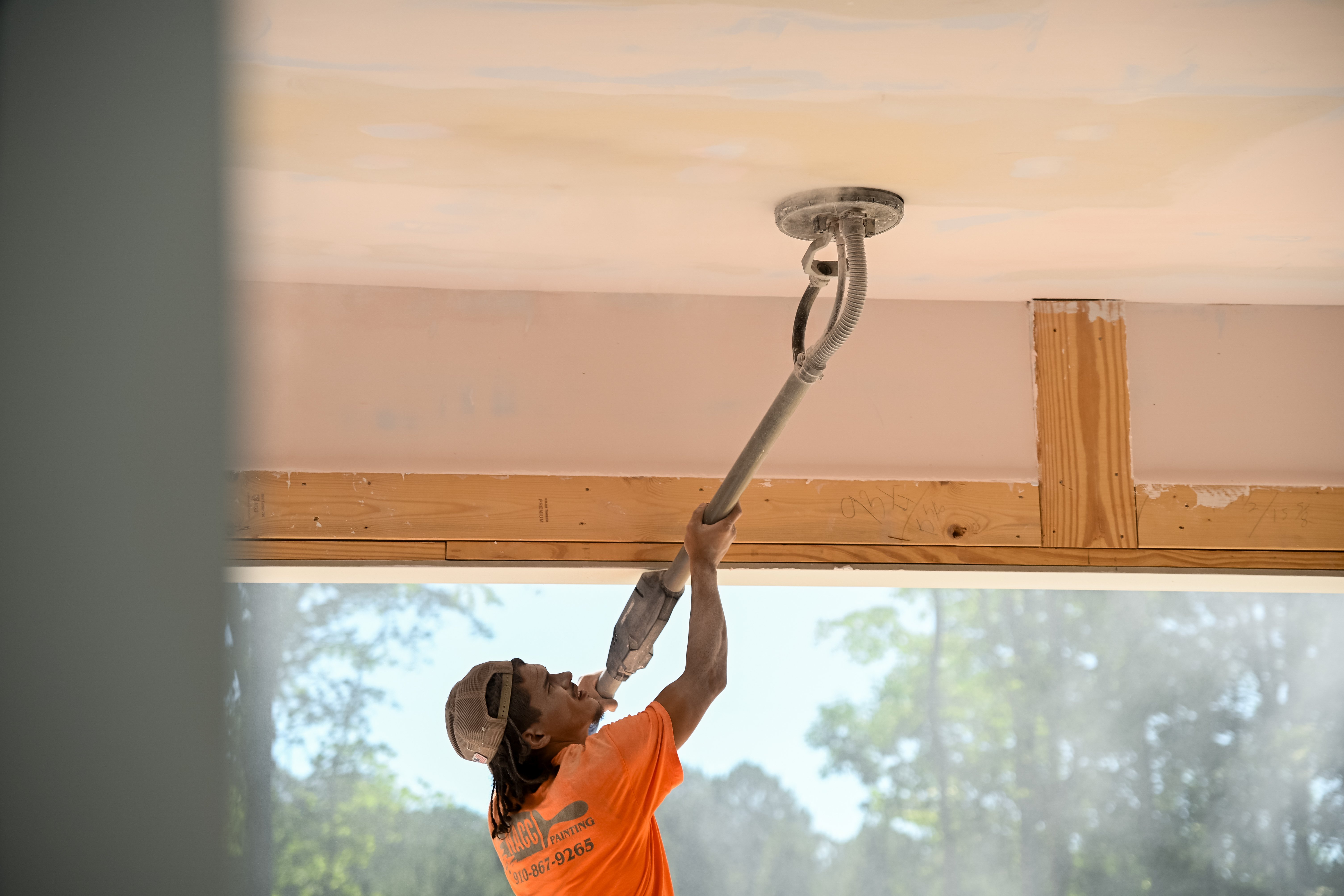 Trabajador de construcción de SEGC lijando el techo de yeso (drywall) durante el proceso de terminación Nivel 5 en la construcción de una casa personalizada