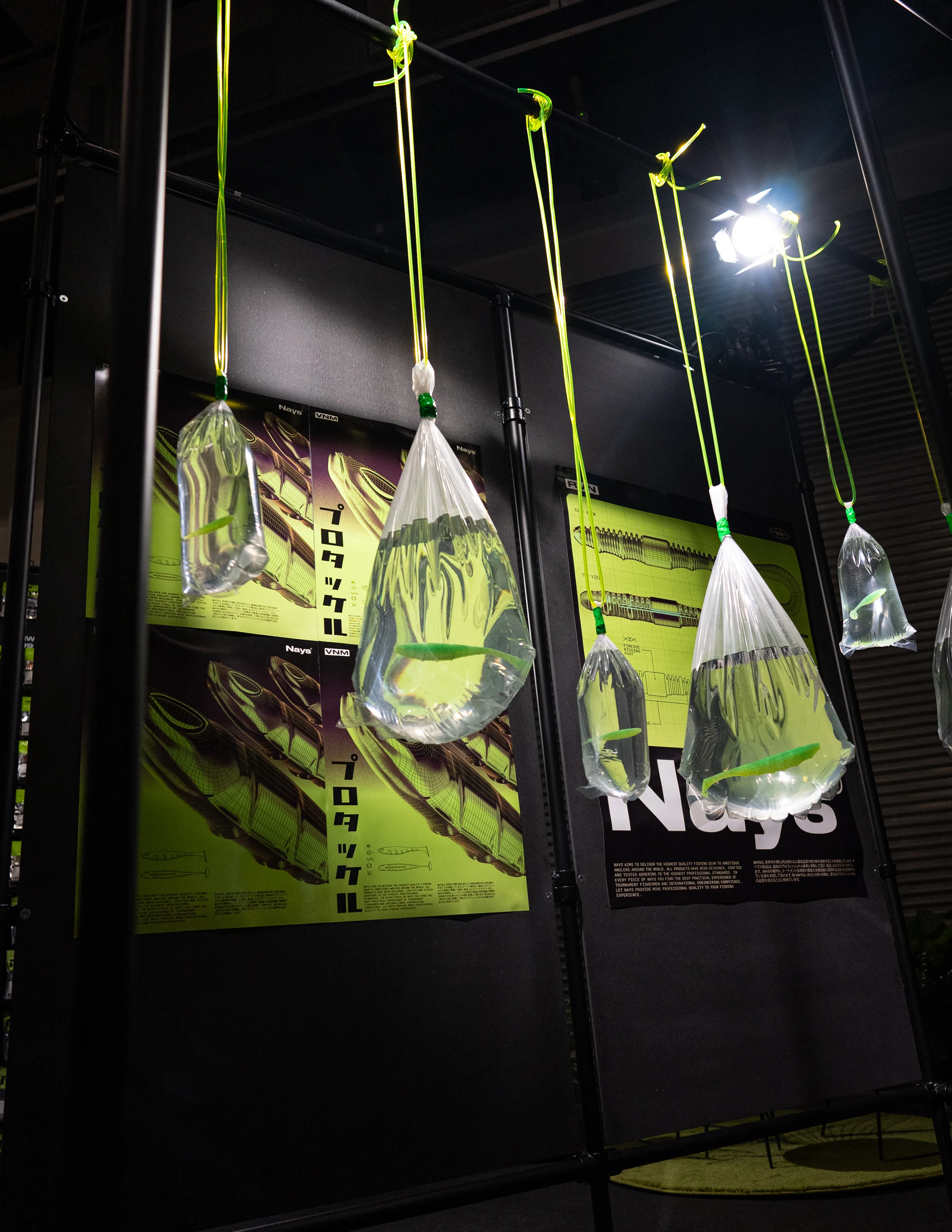 Water-filled plastic bags with neon-green fishing lures hanging from green cords in front of Nays posters.