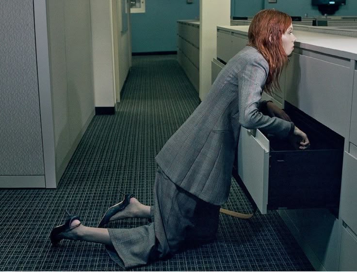 Woman kneeling on the floor digging through an open office file cabinet drawer
