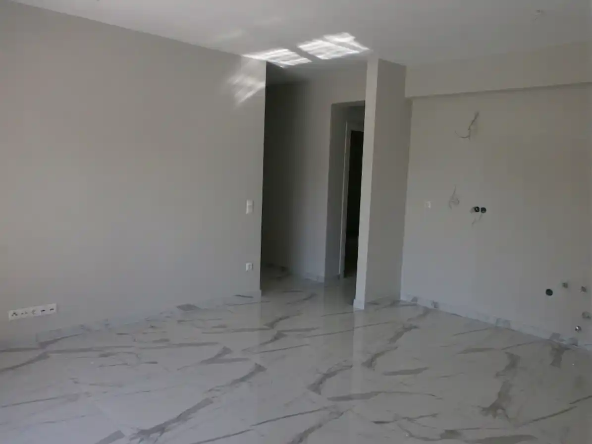 Άδειος εσωτερικός χώρος με λευκούς τοίχους και γυαλιστερά πλακάκια σε όψη λευκού μαρμάρου.