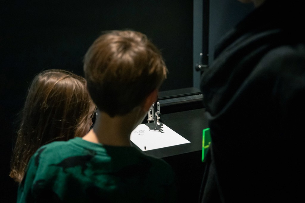 The Bot-I-Celli robot is on exhibition at the Berlin Museum of Communication, where it is drawing a portrait while two children observe it