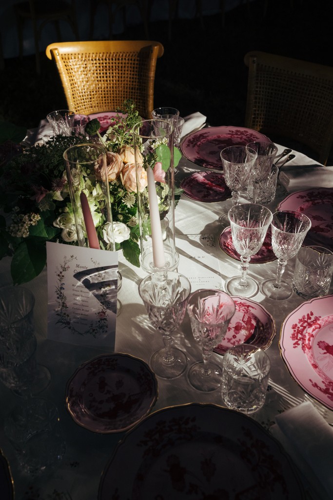 Dettagli tavolo ricevimento con fiori bianchi e rosa, bicchieri di cristallo, sedie dorate e runner bianco su fondo scuro