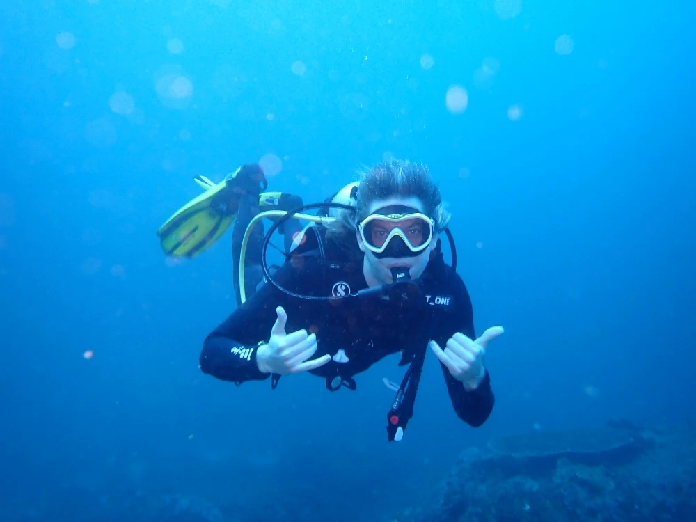 Person wearing a blue puffer jacket and red backpack standing in front of a light blue building on a city street.
