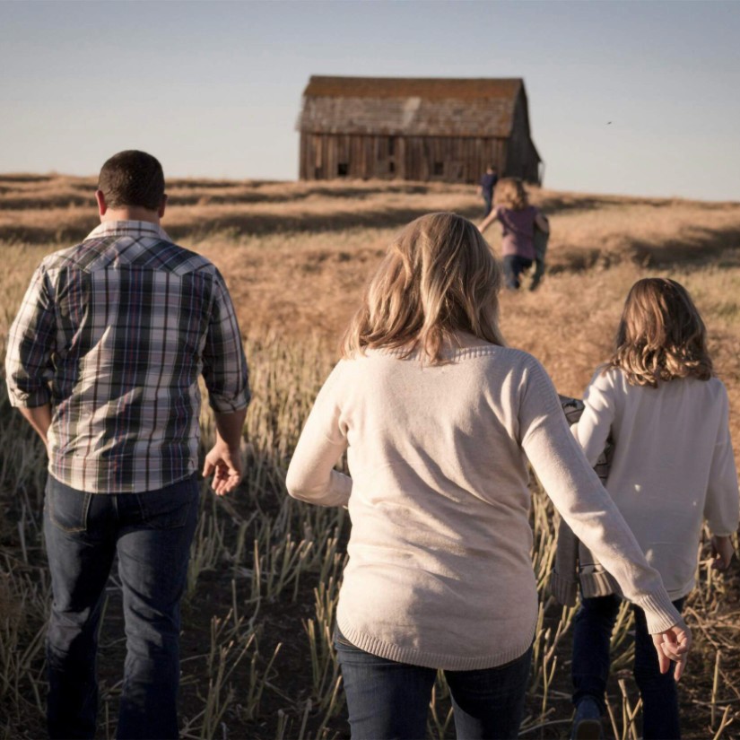 a family walking towards a barn, in a field.