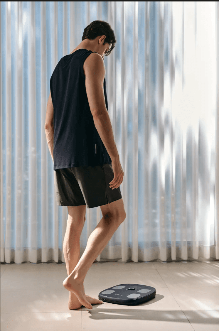 A man in athletic wear preparing to step onto an InBody H30 body composition scale in a bright, modern room.