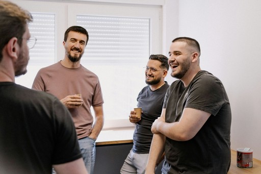 Four men are engaged in conversation in a bright, modern room. One man gestures while others listen.