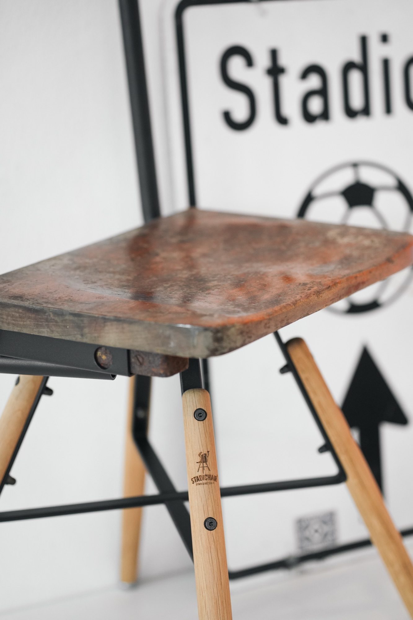Holzhocker mit Metallgestell vor einem Schild, Produktfoto